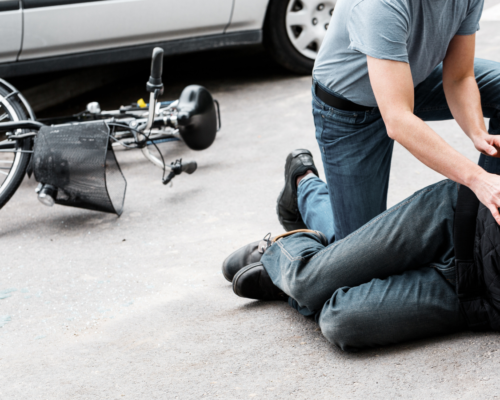 A cyclist lies injured on a Dallas roadway beside a fallen bicycle while another person provides assistance, illustrating the risks of unsafe passing and the importance of the Dallas 3 foot passing law in bicycle accident claims.